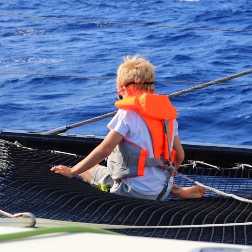 enfant assis sur le trampoline du catamaran de François Gabart